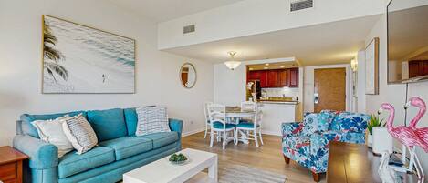 A modern living room with a blue sofa, a white coffee table, and a dining area with a white table and chairs.