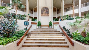 Un vestíbulo de hotel con una escalera central, rodeado de exuberante vegetación y palmeras.