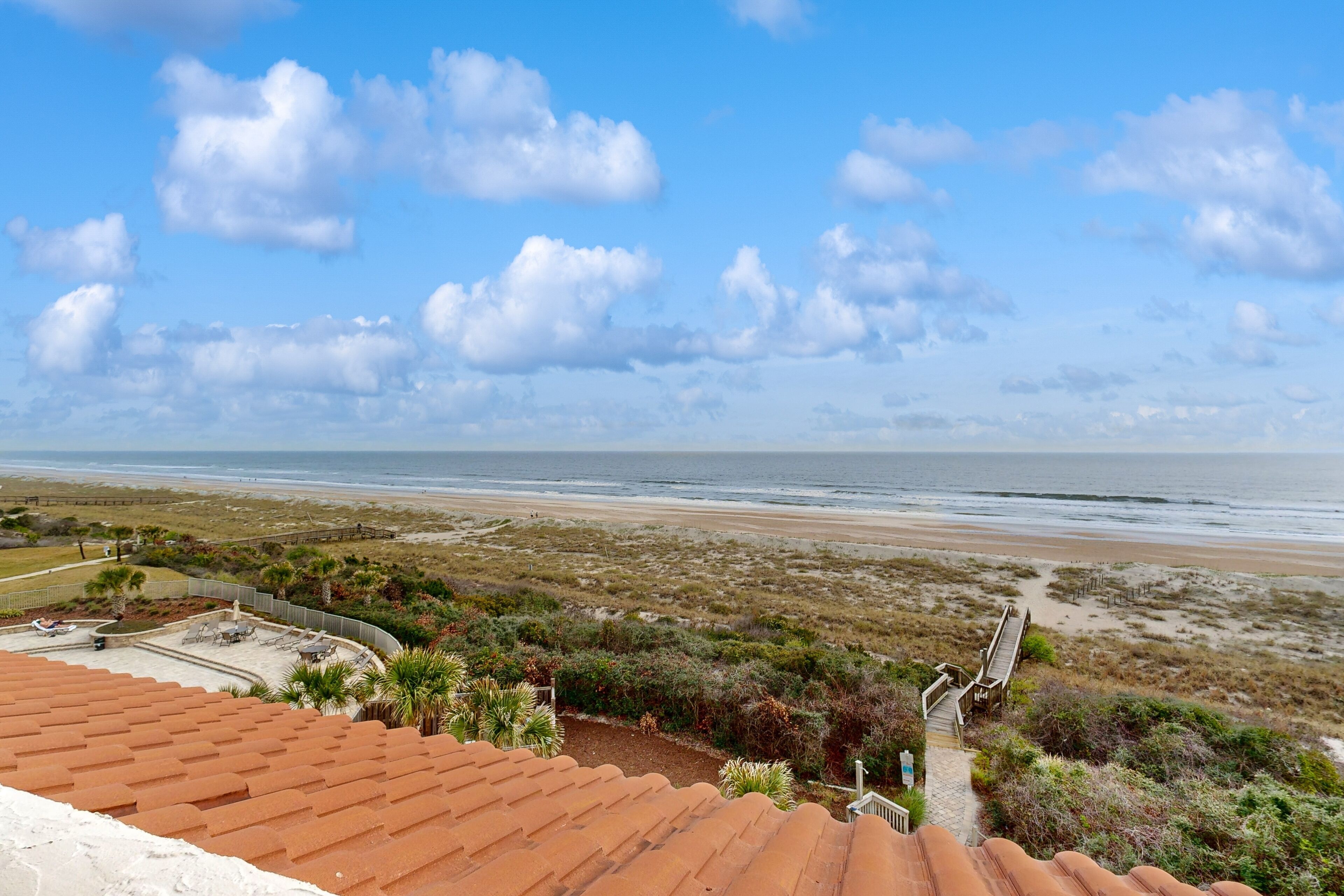 Une vue sur la plage depuis une terrasse surmontée d’un toit rouge, avec une plage de sable et un ciel dégagé.