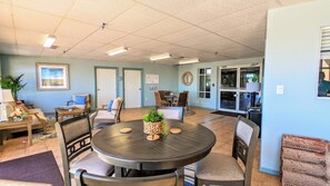 A dining area with a round table, chairs, and a plant centerpiece. There are doors and a window in the background. - Blue Horizon at Surf Club - Ocean Views 3rd Floor Corner Wraparound Balcony! (Palm Coast)
