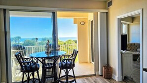 A balcony with a glass table and chairs, a view of the ocean, and a wicker basket. - Blue Horizon at Surf Club - Ocean Views 3rd Floor Corner Wraparound Balcony! (Palm Coast)