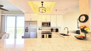 A modern kitchen with stainless steel appliances, a marble countertop, and a view to the outside. - Blue Horizon at Surf Club - Ocean Views 3rd Floor Corner Wraparound Balcony! (Palm Coast)