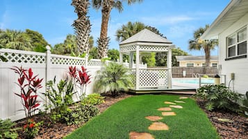 Un jardin bien entretenu avec une pelouse, des dalles de pierre, un kiosque et une piscine.