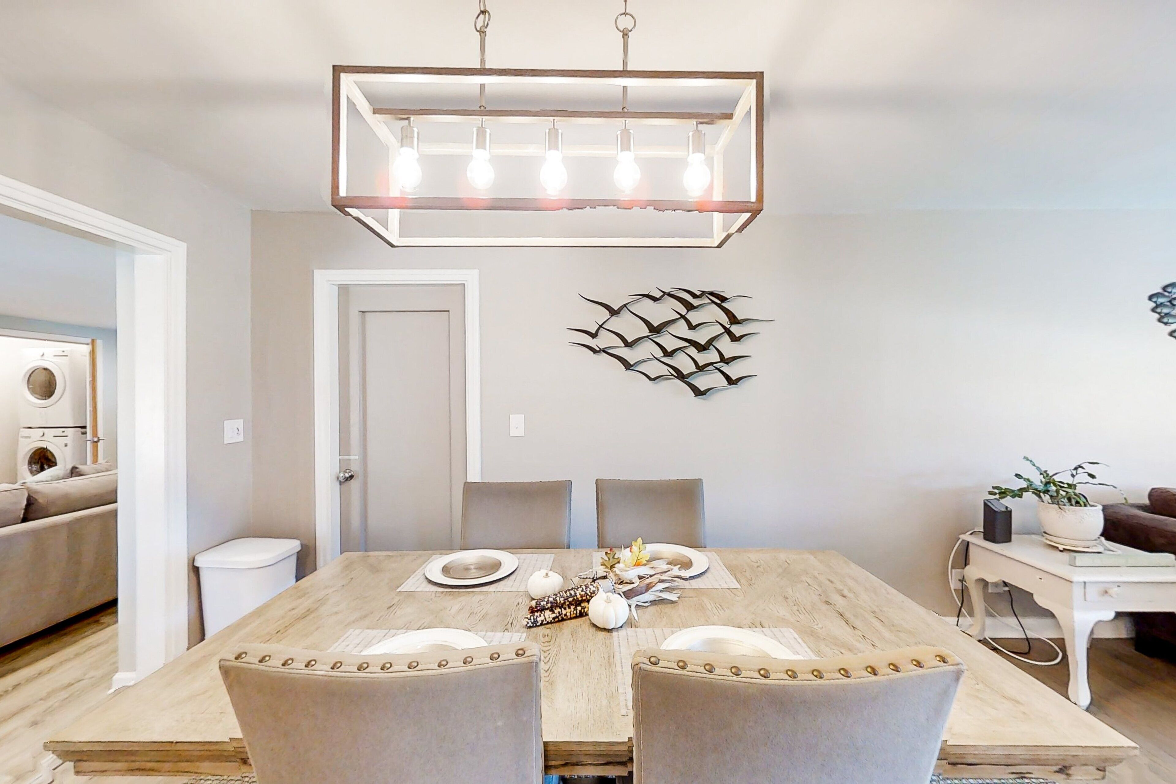 Un coin repas avec une table en bois dressée pour quatre personnes, un lustre moderne et un élément décoratif mural.