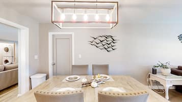 Un coin repas avec une table en bois dressée pour quatre personnes, un lustre moderne et un élément décoratif mural.