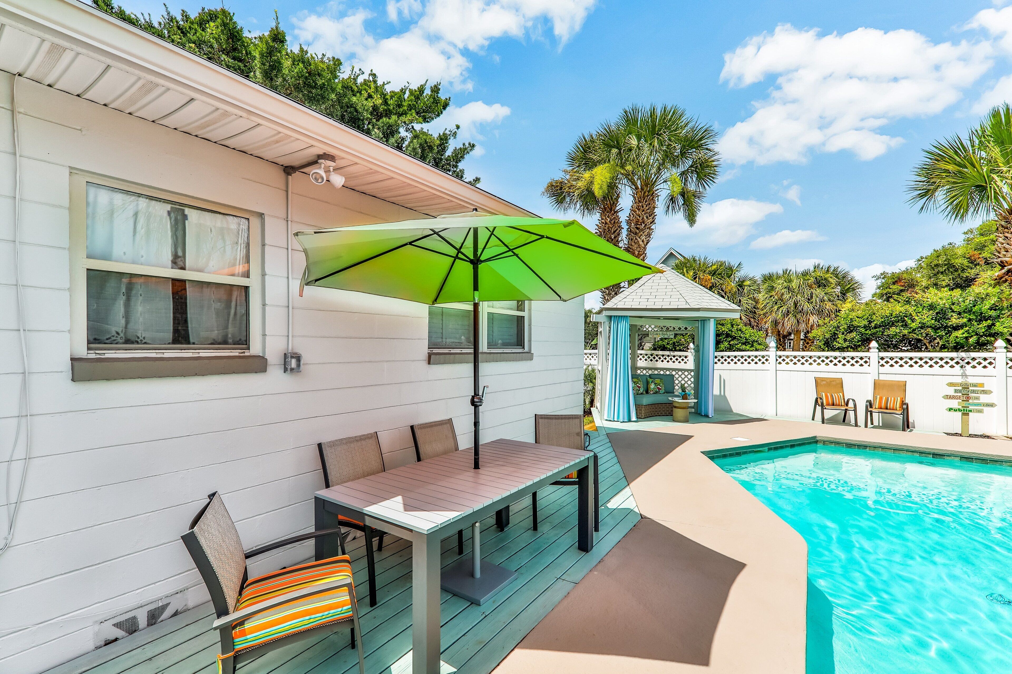 Un espace aménagé au bord de la piscine, avec une terrasse en bois, une table et des chaises, et un parasol vert.