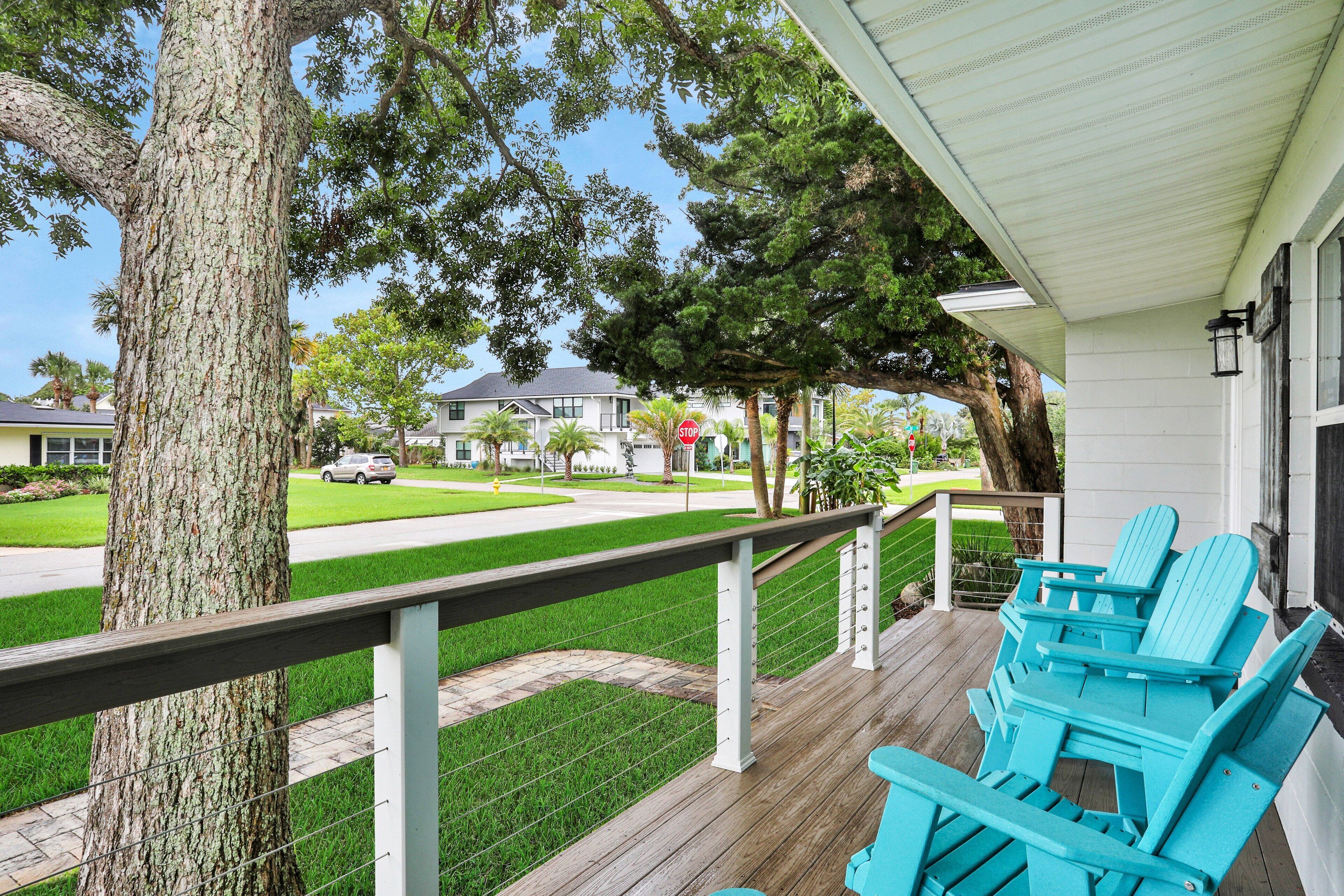 Une véranda avec une balustrade en bois, un arbre et des chaises Adirondack bleues.