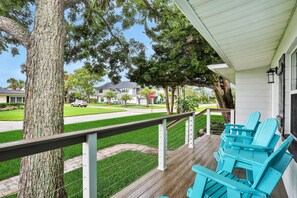 Eine Veranda mit Holzgeländer, einem Baum und blauen Adirondack-Stühlen.