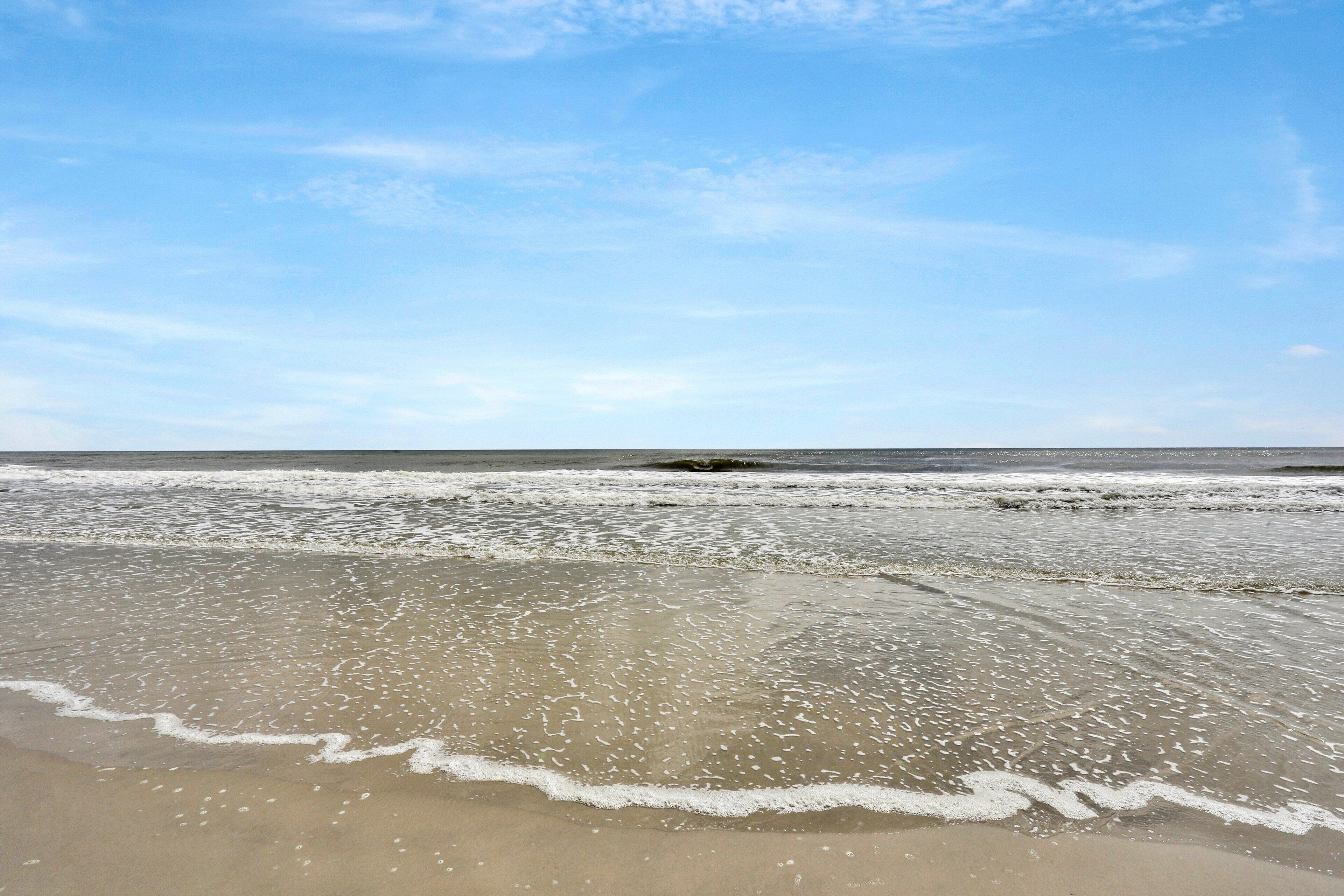 Une plage où les vagues viennent doucement lécher le rivage sous un ciel dégagé.
