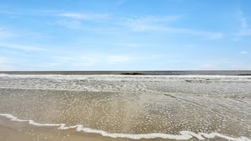 Une plage où les vagues viennent doucement lécher le rivage sous un ciel dégagé.