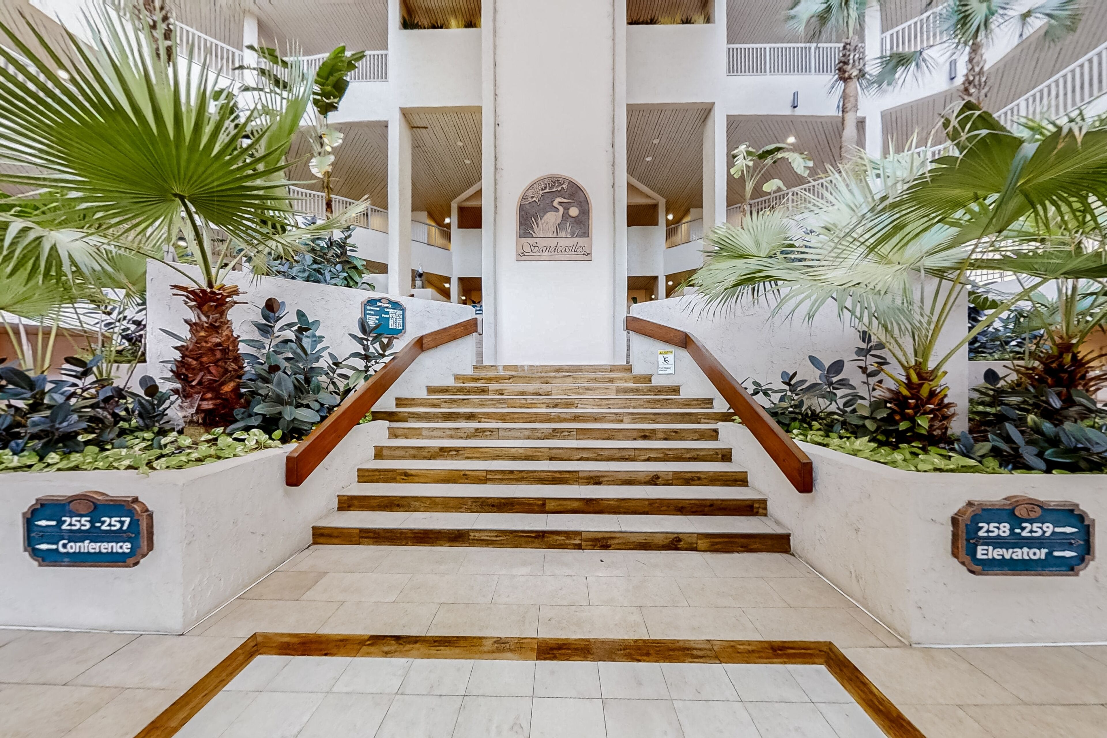 Una escalera con escalones de madera y barandilla, flanqueada por macetas con plantas tropicales.
