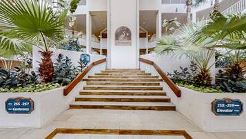 Un escalier avec des marches en bois et une rampe, bordé de jardinières contenant des plantes tropicales.