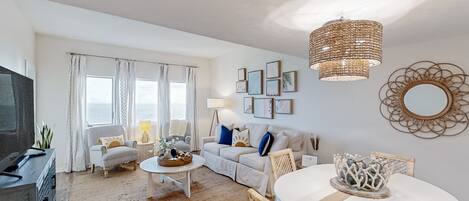 A living room with a sofa, coffee table, and dining table. There is a television, a lamp, and a decorative mirror on the wall.