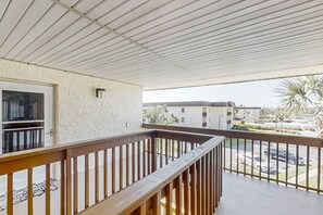 A balcony with a wooden railing, a white textured wall, and a view of a parking lot and buildings in the background. - 3rd-floor Condo W/fountain Views, Private Balcony & W/d, On-site Pool & hot Tubs (St. Augustine)