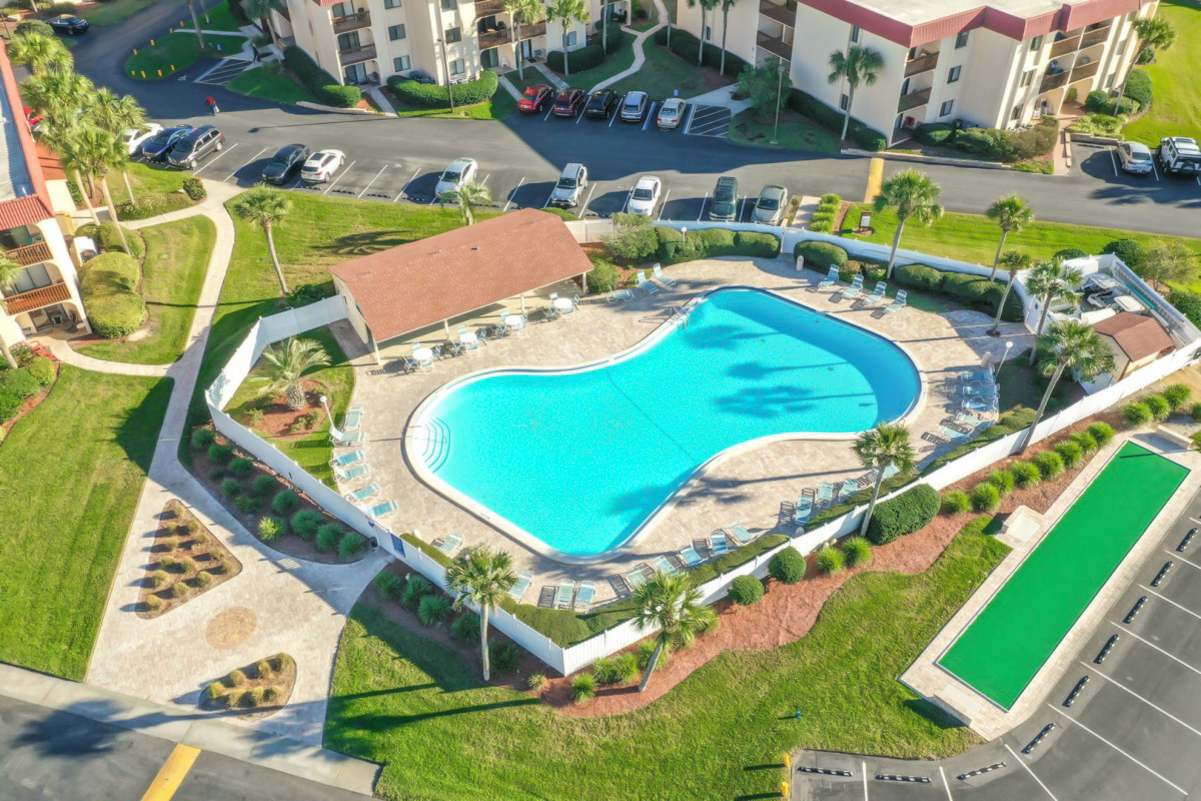 Vue aérienne d’un hôtel doté d’une grande piscine, de plusieurs parkings et d’un espace vert environnant.
