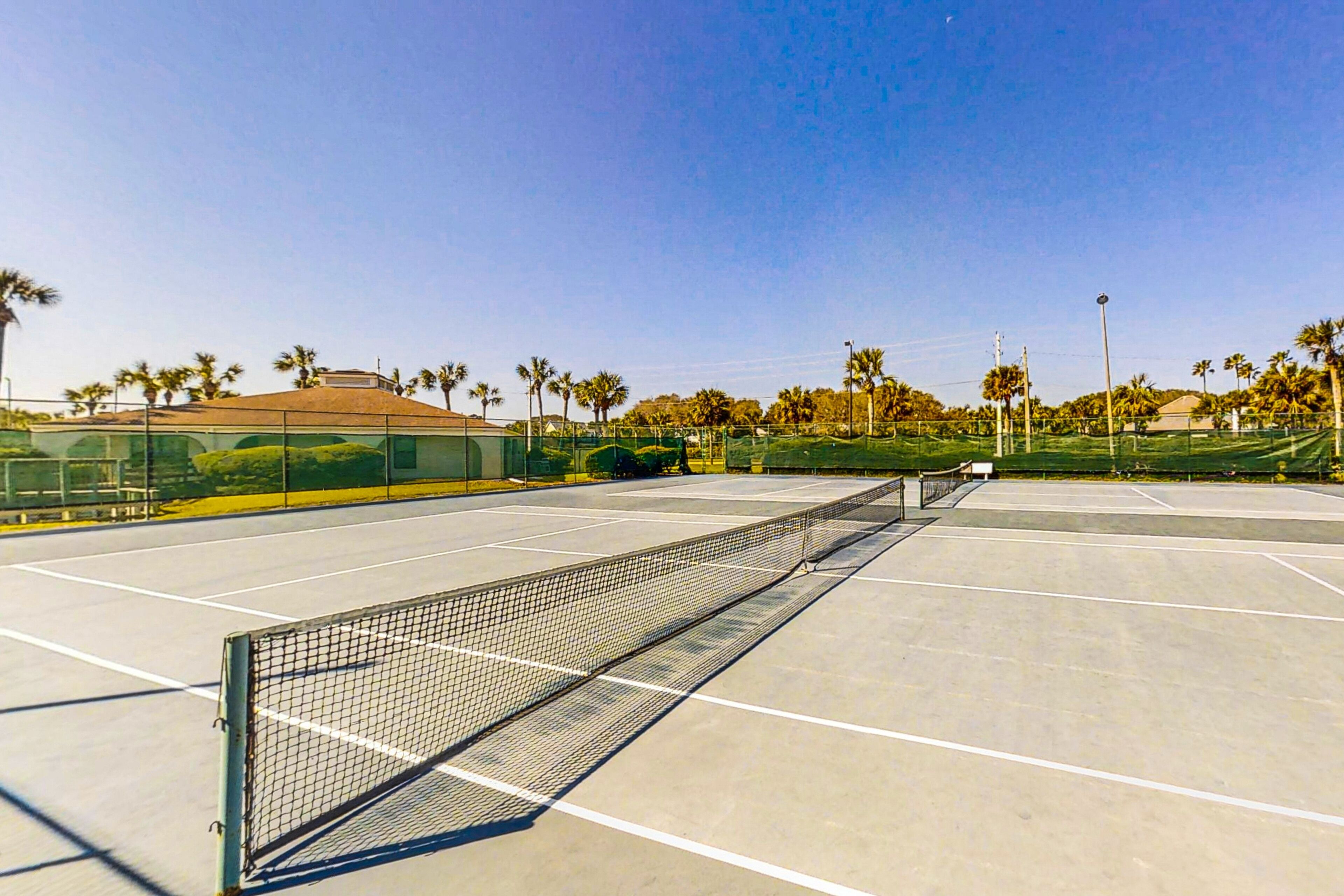 Ein Tennisplatz mit Netz, umgeben von Palmen und einem Gebäude im Hintergrund.
