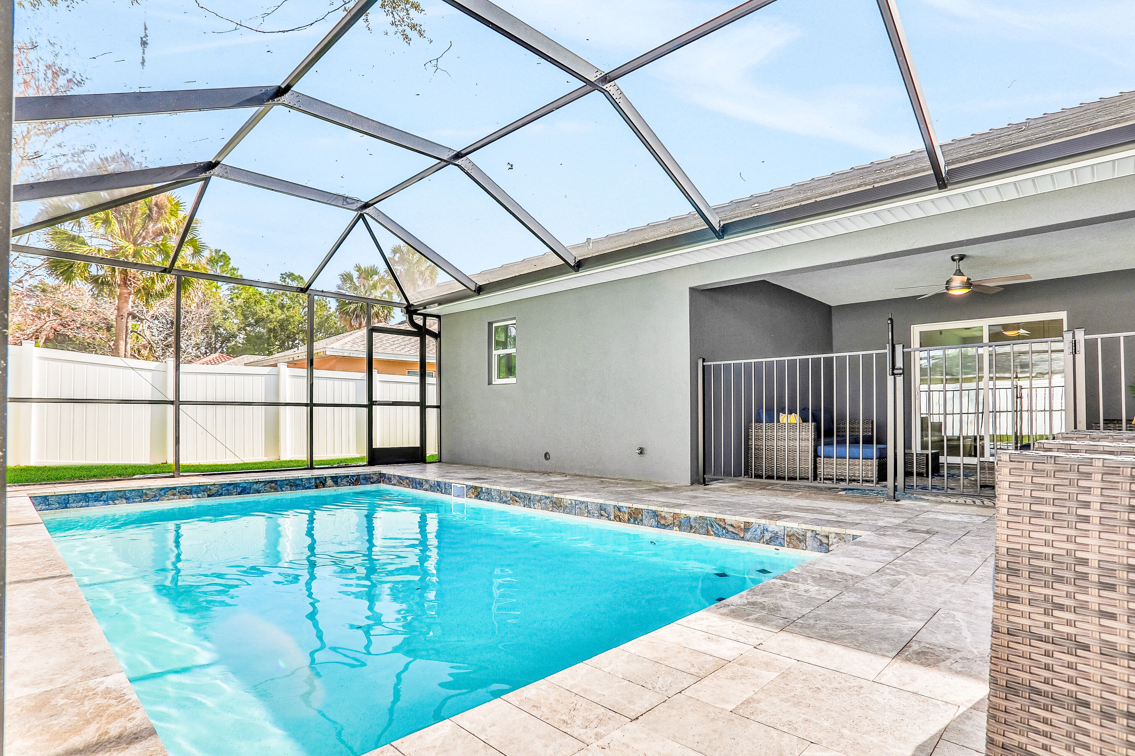 Una piscina con techo de vidrio, rodeada por una zona de patio con valla blanca y una silla de mimbre.