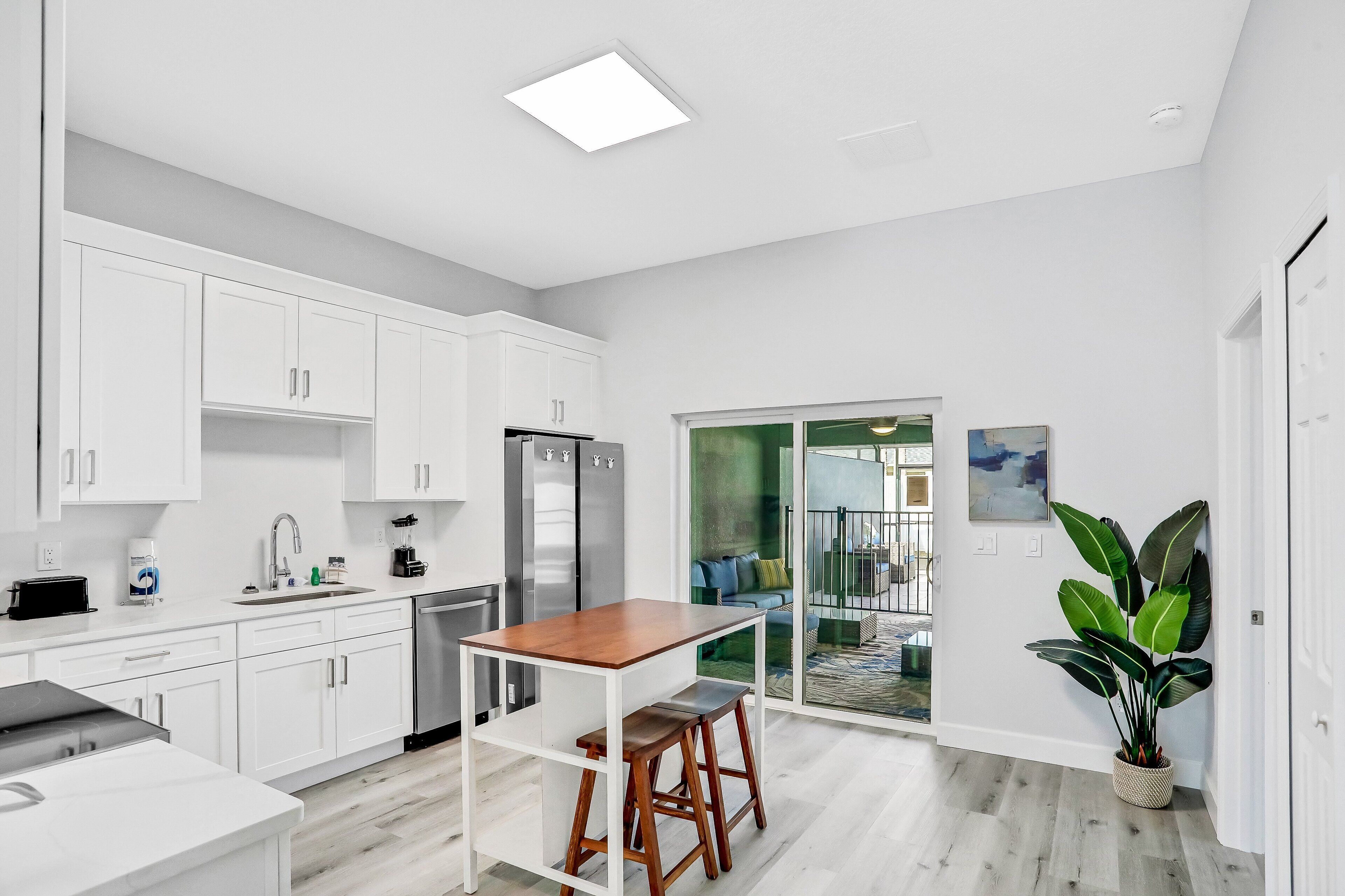 A modern kitchen with white cabinets, a wooden table, and a large plant.