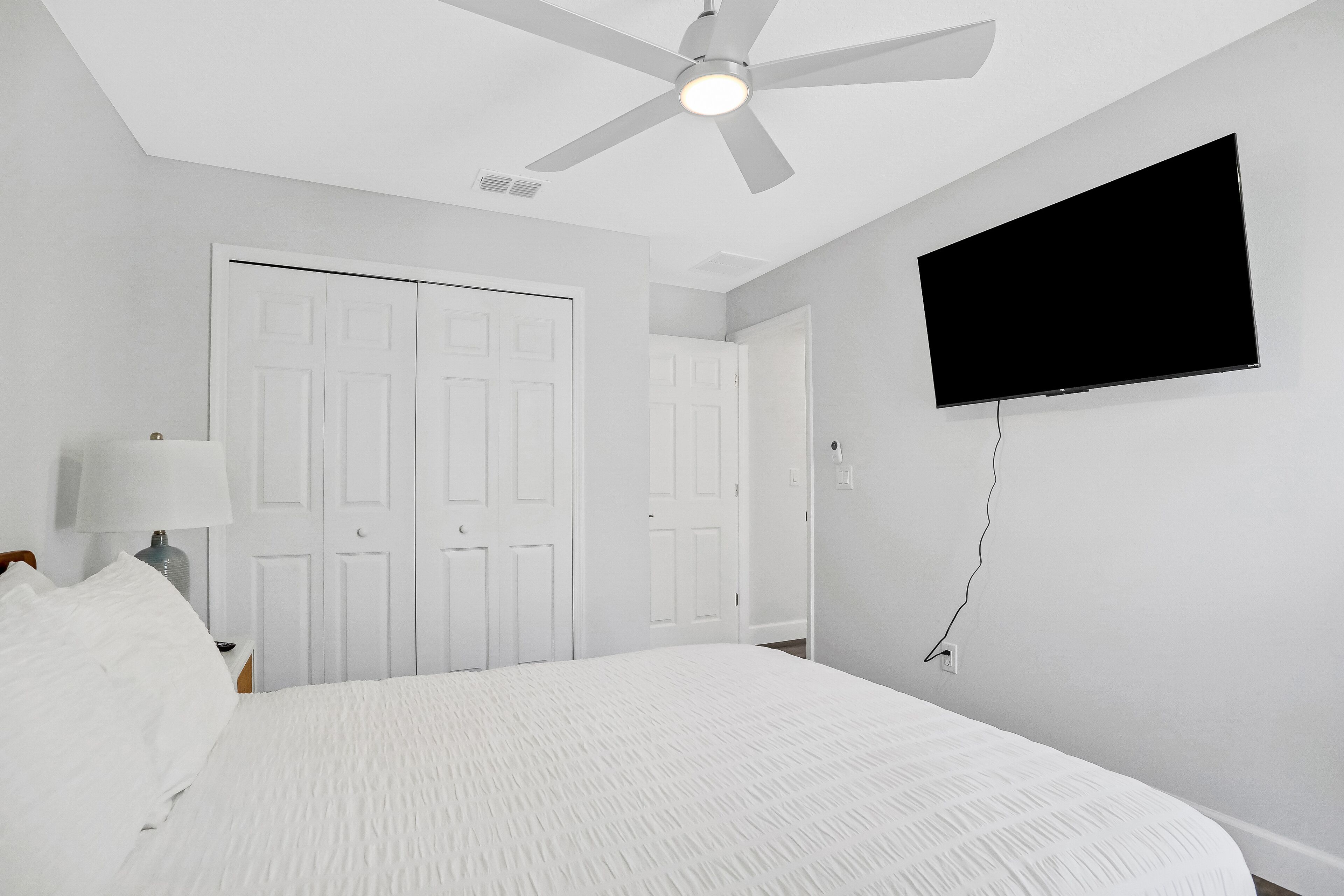 Una camera da letto con un letto, un ventilatore a soffitto, una TV e porte bianche.
