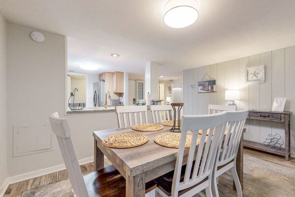 A dining area with a wooden table, white chairs, and woven placemats. - Dog-friendly Beach Wood Villa Across the Street From the Beach With Pool (Fernandina Beach)