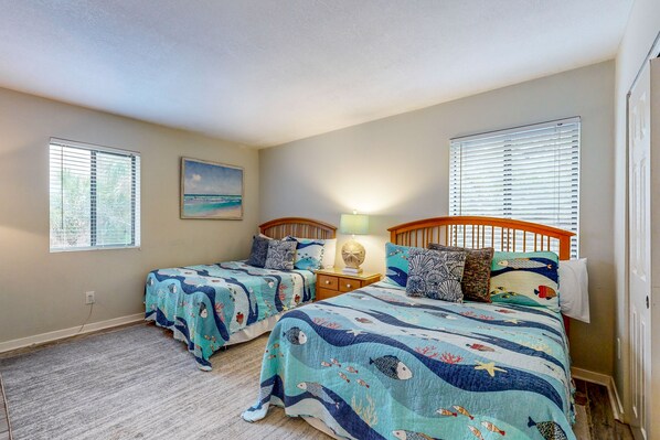 A bedroom with two beds, a nightstand, a lamp, and a painting on the wall. - Dog-friendly Beach Wood Villa Across the Street From the Beach With Pool (Fernandina Beach)