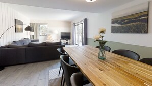 Una sala de estar moderna con una mesa de comedor de madera, un sofá gris y un ventanal grande.