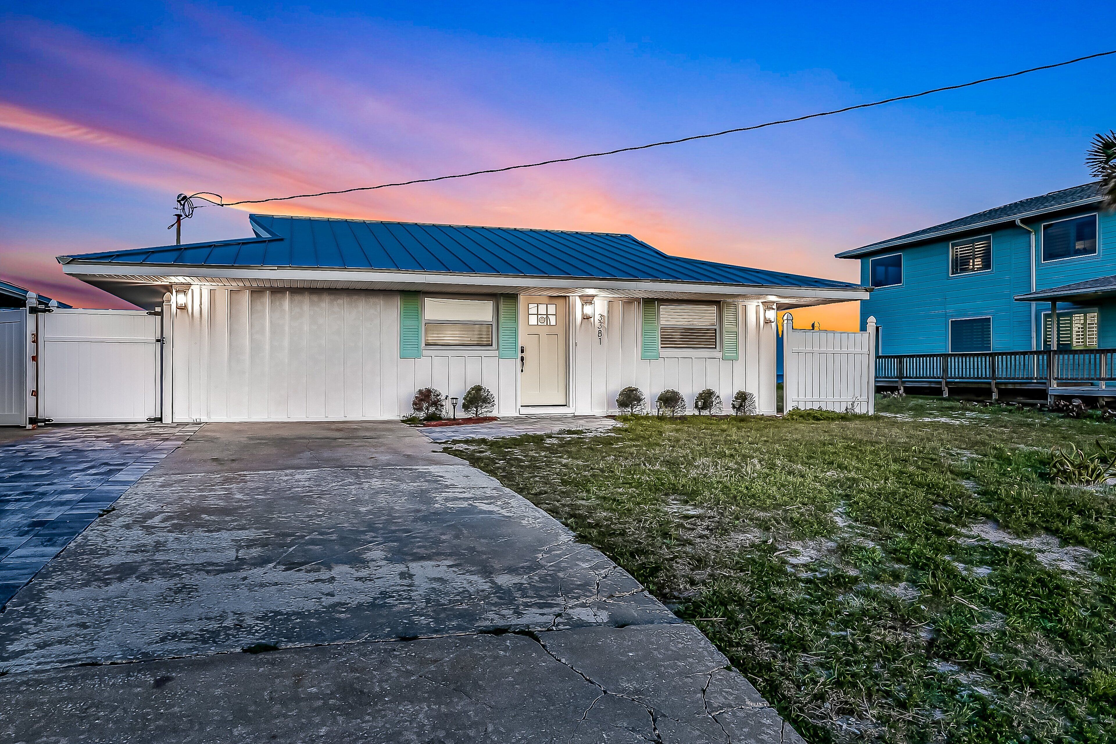 A single-story house with a blue roof, a front porch, and a small front yard.