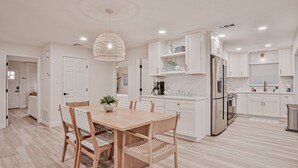 A modern kitchen with white cabinetry, a wooden dining table, and a hanging light fixture. - Beachfront Home w/ Private Lanai and Deck - Walk to the Beach (Flagler Beach)