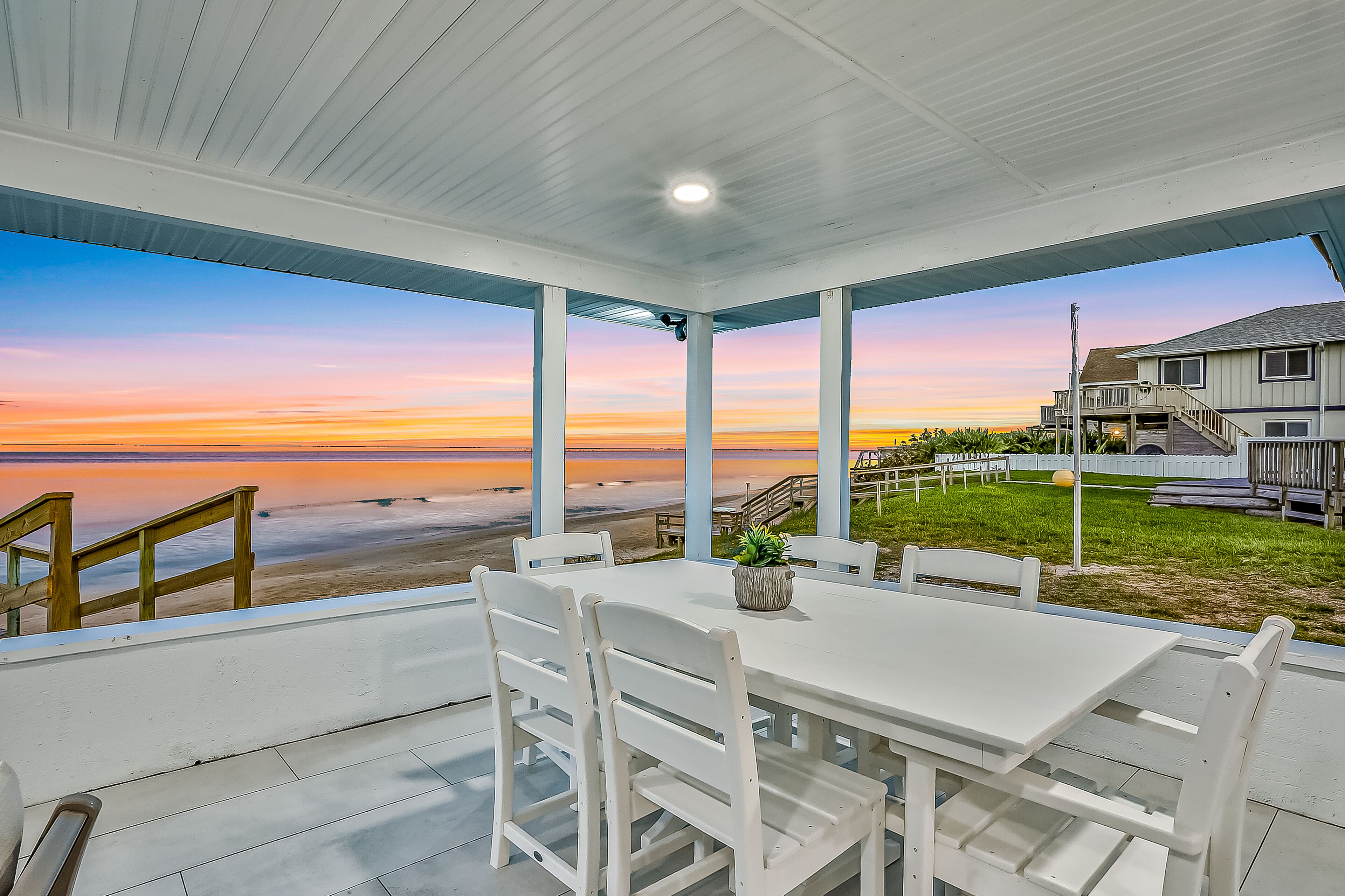 A covered patio with a view of the beach and ocean at sunset.