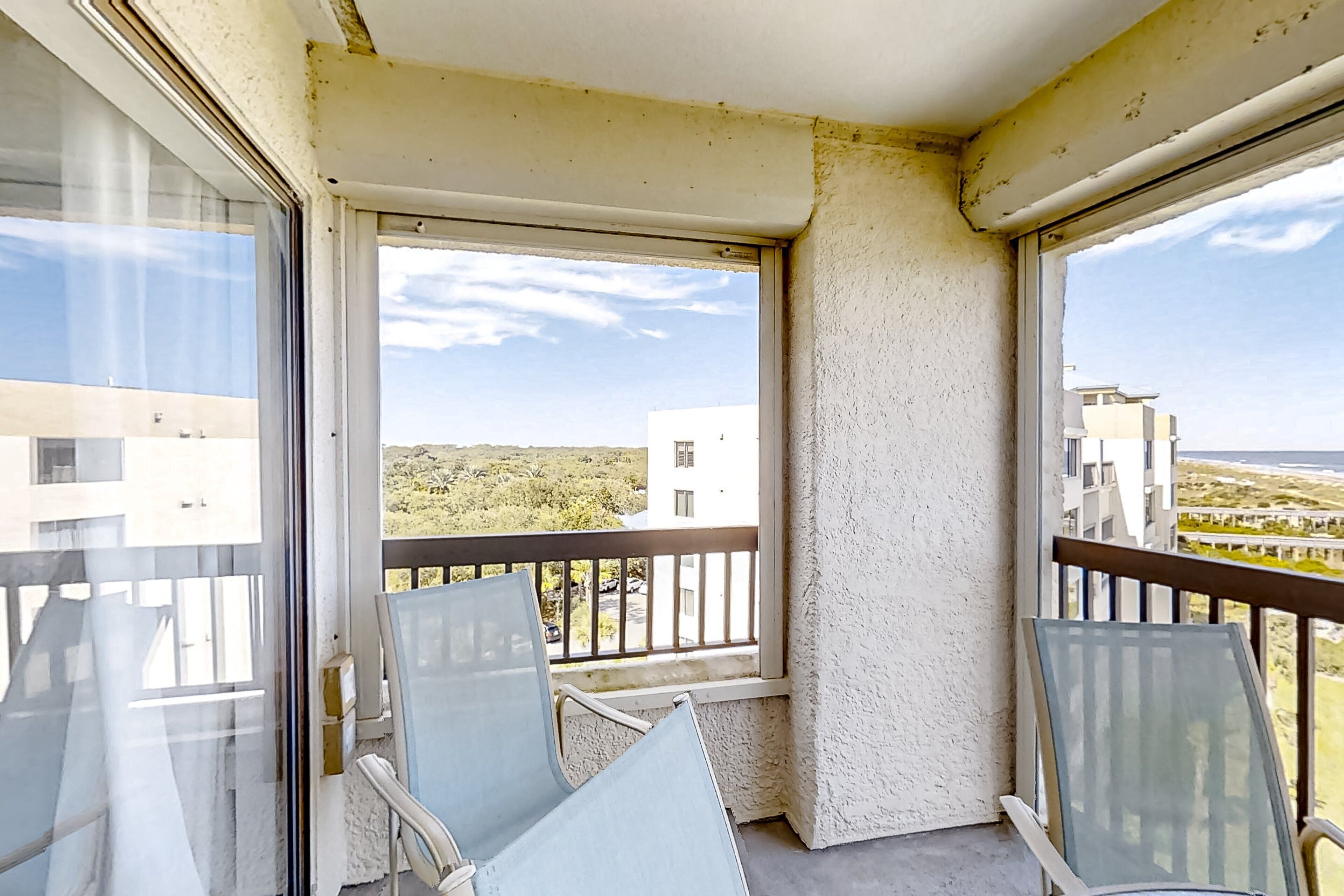 A balcony with two chairs, a view of buildings, and a clear sky.