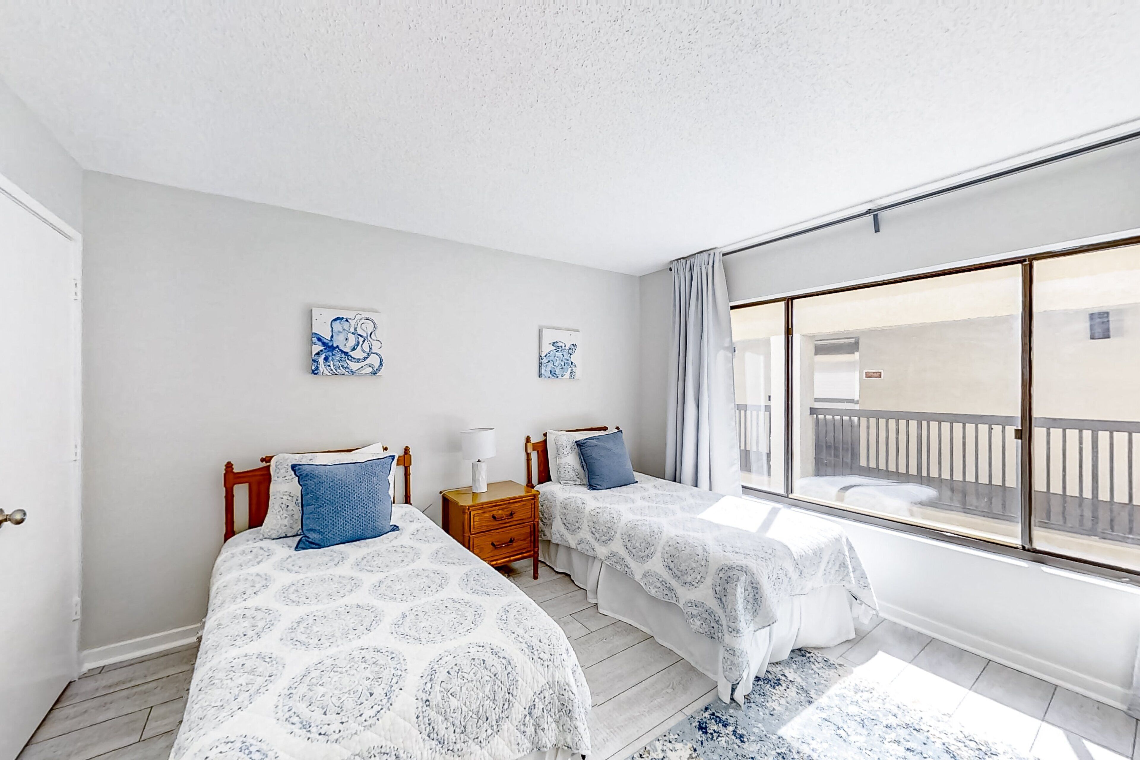 A bedroom with two beds, a nightstand, and a large window with a view of a balcony.