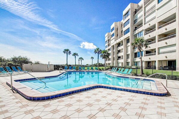 A swimming pool with a tiled deck, surrounded by lounge chairs and a multi-story building with balconies. - Condo With Shared Pool, Beach Access and Spectacular Atlantic Ocean Views (Fernandina Beach)
