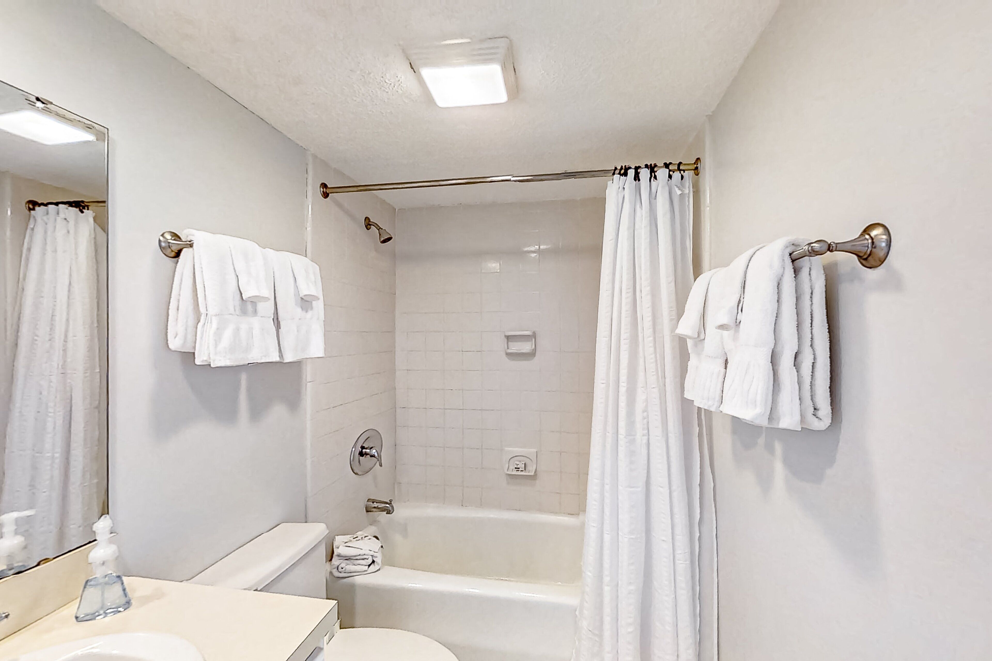 Ein Badezimmer mit einer Badewanne, einer Toilette und einem Waschbecken. Handtücher hängen an der Wand und eine Duschvorhang ist angebracht.
