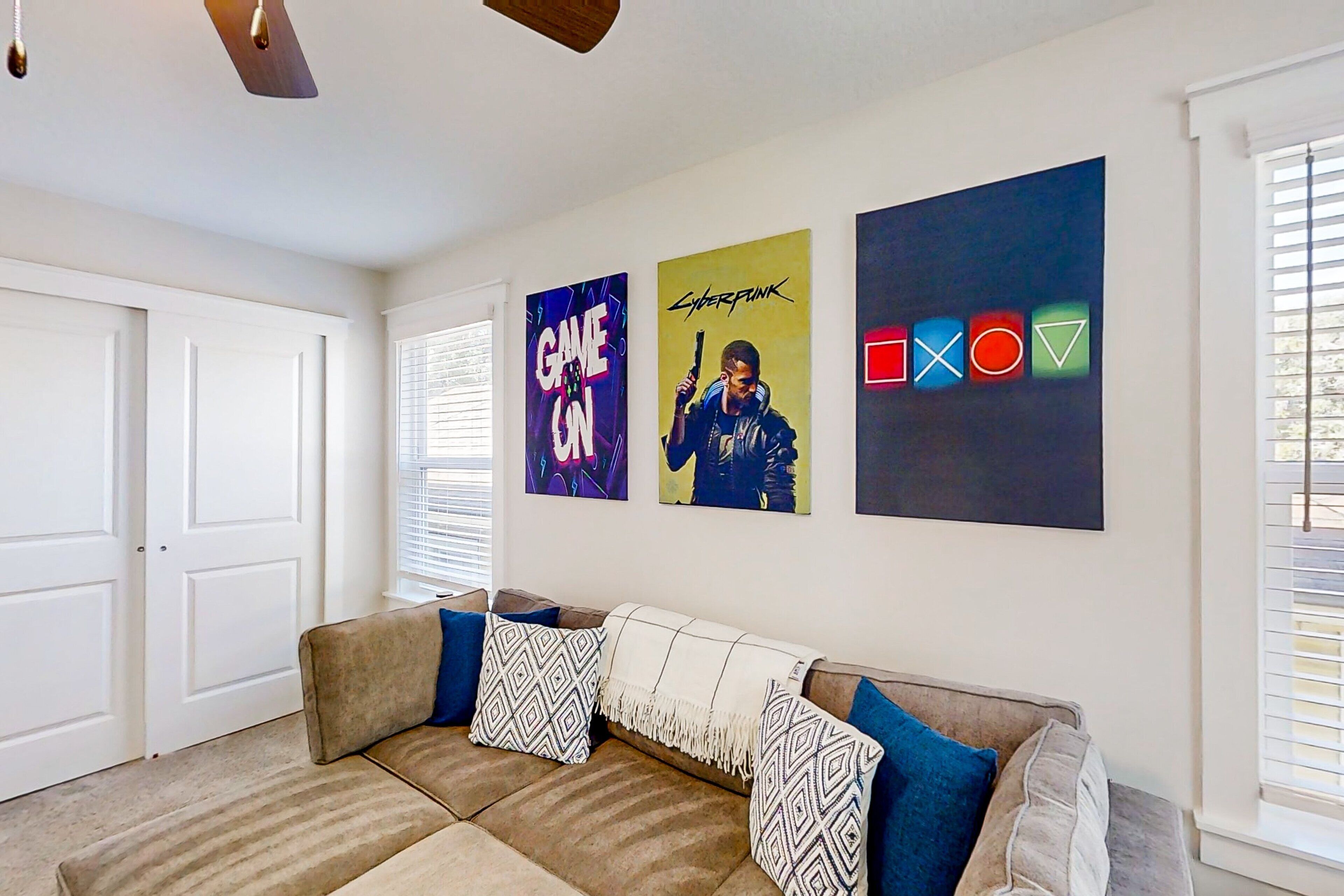 A living room with a beige sectional sofa, patterned throw pillows, and three framed posters on the wall.
