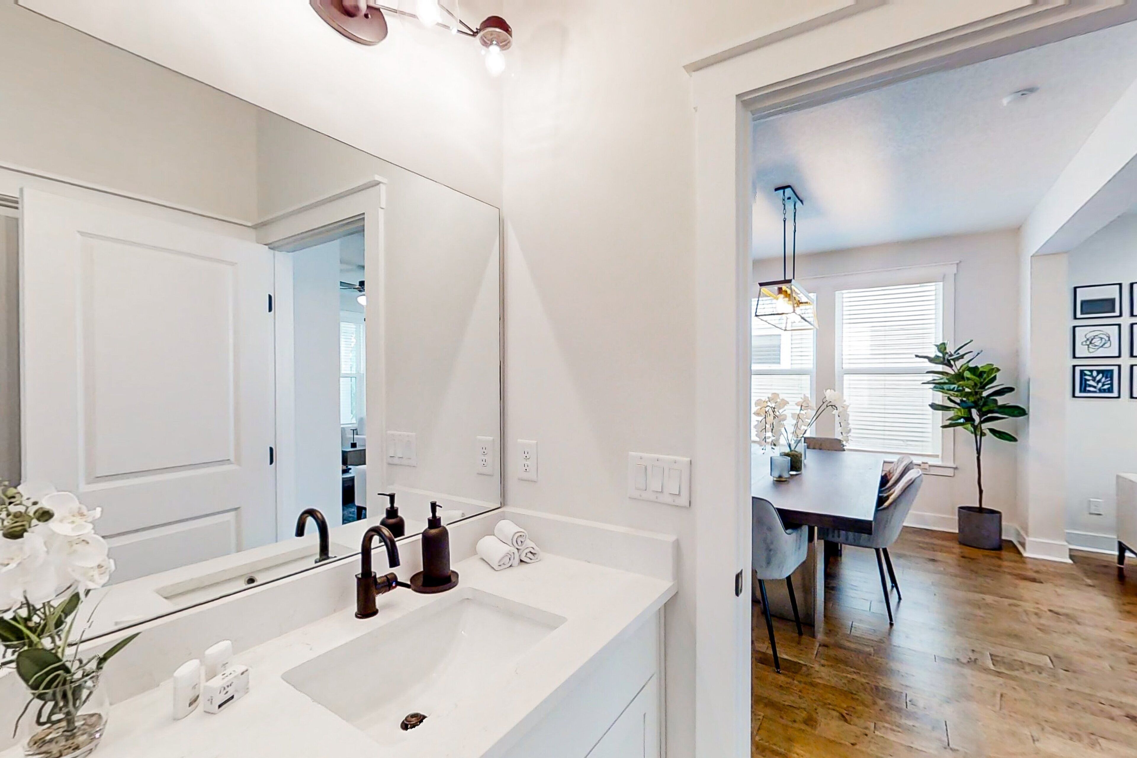 Un baño moderno con un espejo grande, lavamanos blanco y zona de ducha.