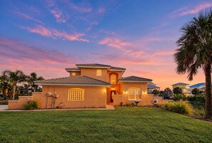 A two-story house with a well-maintained lawn, a palm tree, and a sunset sky. - Coral Casa - Amazing Pool House Next to the Beach! 3 Min Walk! Awesome Pool! (Palm Coast)