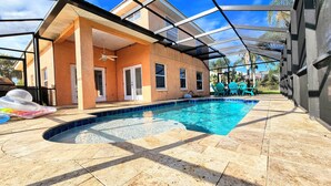 A covered swimming pool area with a house in the background, clear skies, and a patio with chairs. - Coral Casa - Amazing Pool House Next to the Beach! 3 Min Walk! Awesome Pool! (Palm Coast)