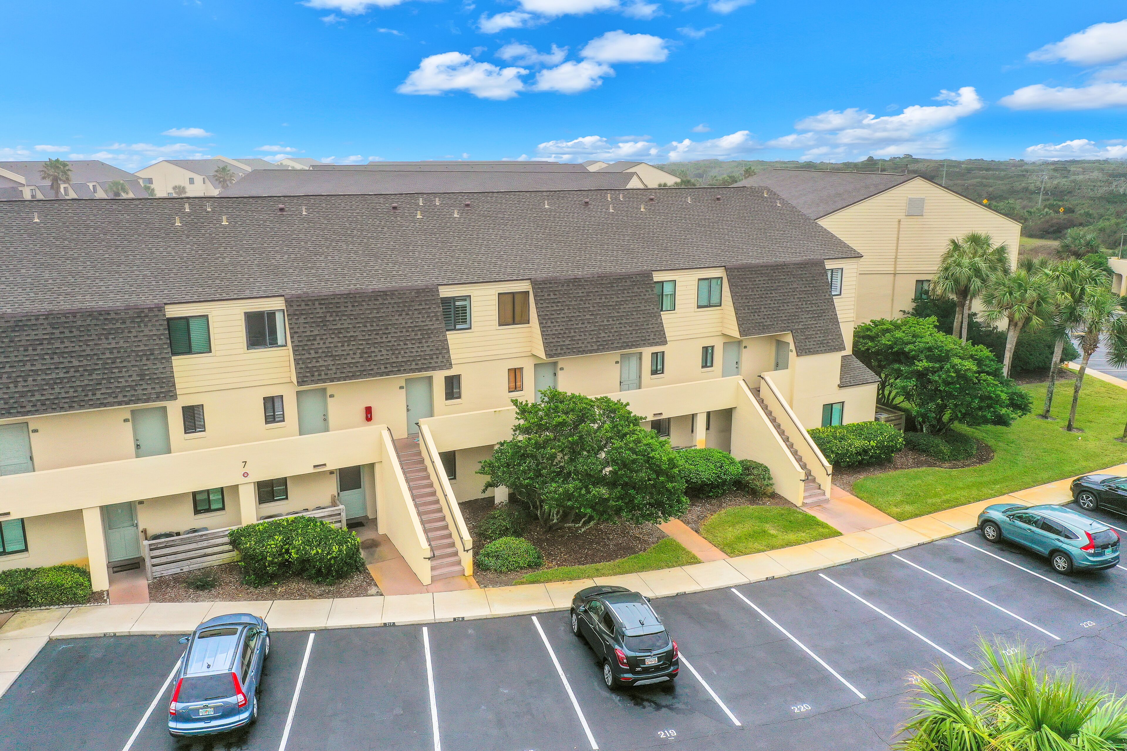 A multi-story residential building with a parking lot, a staircase, and a small garden area.
