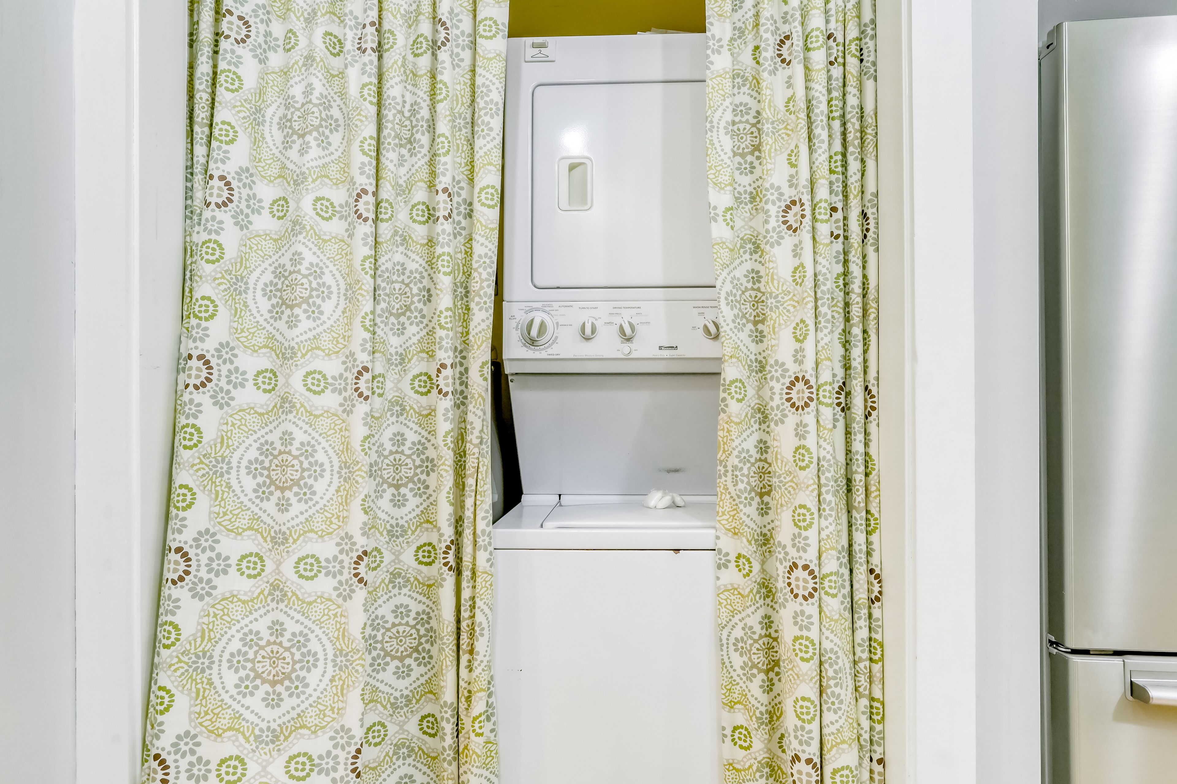 A compact laundry room with a washing machine and dryer, enclosed by patterned curtains.