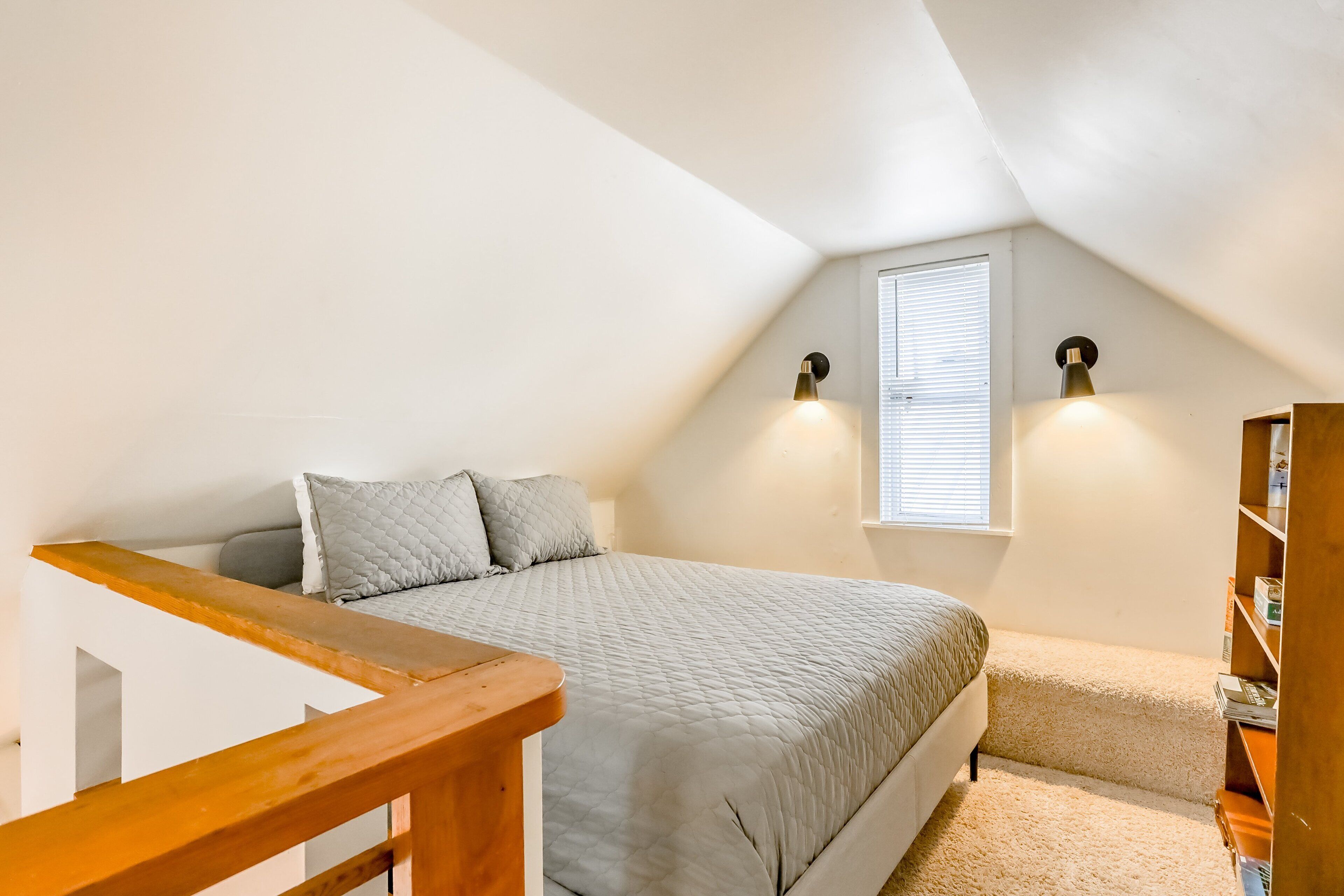 A bedroom with a bed, a wooden bench, a bookshelf, and two wall-mounted lights.