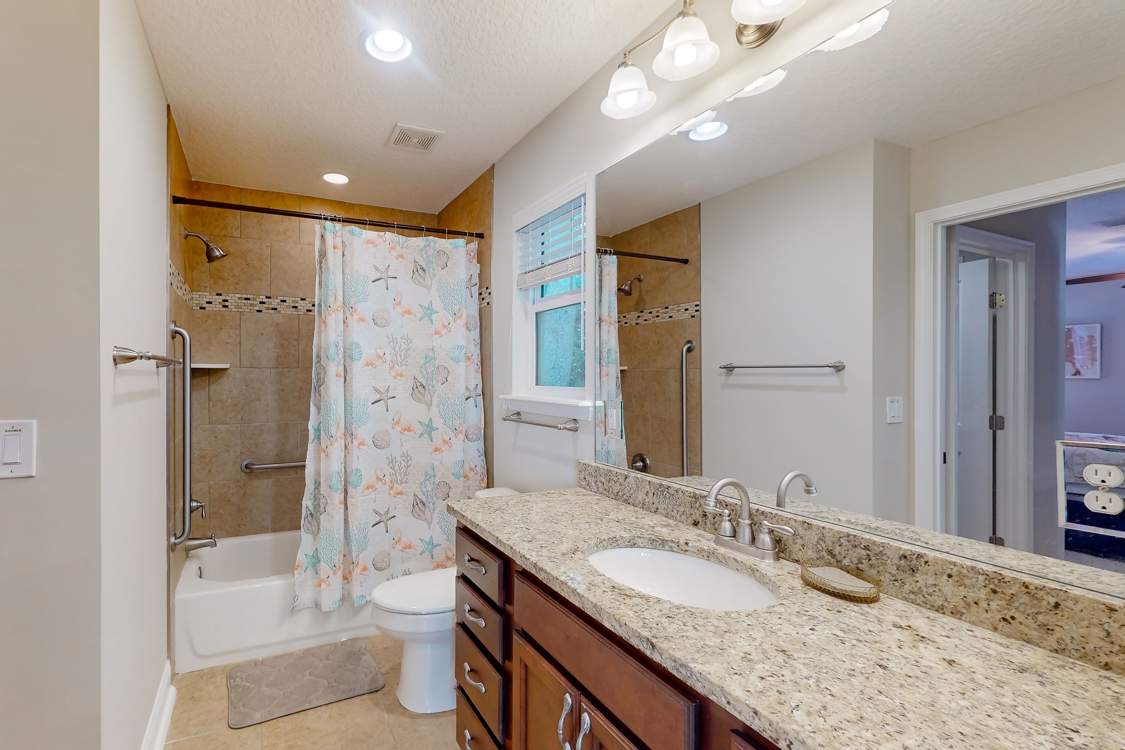 A bathroom with a shower, toilet, and sink, equipped with grab bars and a large mirror.