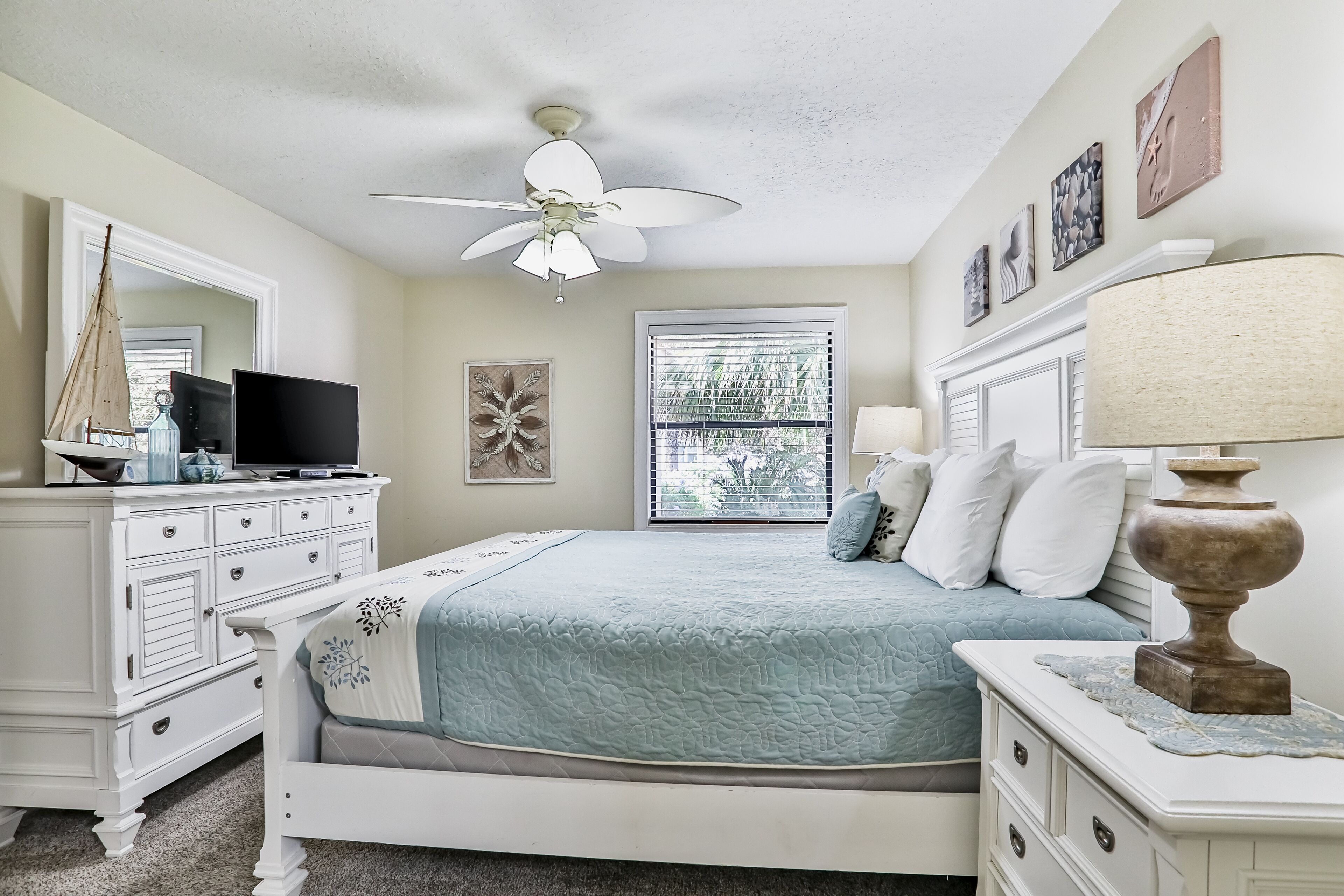 A bedroom with a bed, dresser, television, and ceiling fan.