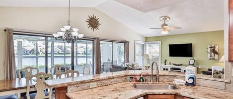 A spacious kitchen with a large island, a dining area with chairs, and a view of a body of water through large windows.