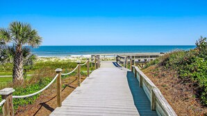 Une promenade en bois qui mène à une plage, avec un ciel bleu dégagé.