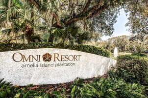 A sign for Omni Resort Amelia Island Plantation with lush greenery and a fountain in the background.