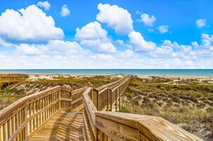 A wooden boardwalk leading to a beach with a clear sky and clouds.