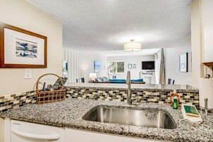 A kitchen with a granite countertop, stainless steel sink, and a wicker basket with utensils.