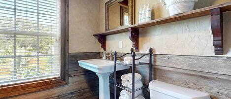 Un baño con suelo de madera, lavamanos pedestal, inodoro y toallero.