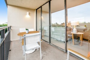 En balkong med ett bord och stolar, en glasdörr som leder in till ett inomhusområde med en soffa och en lampa.
