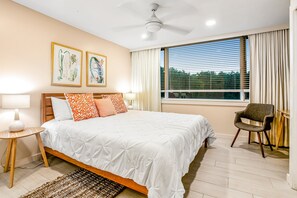 Une chambre à coucher comprenant un lit, deux lampes fixées au mur, un ventilateur de plafond, une fenêtre avec des stores et une chaise.